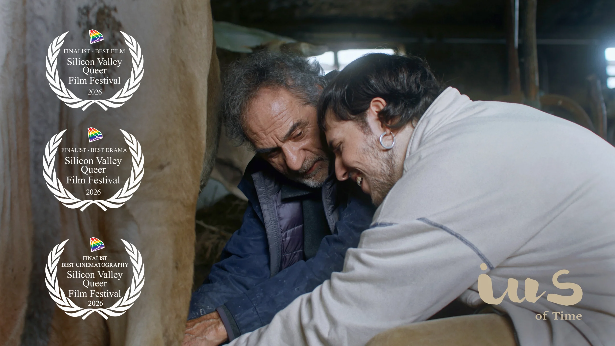 Film still from the short film “IUS of Time” showing Xuan and Luca milking a cow and smiling inside a barn, featuring finalist laurels for Best Film, Best Drama, and Best Cinematography at the 4th Silicon Valley Queer Film Festival, United States, 2026.