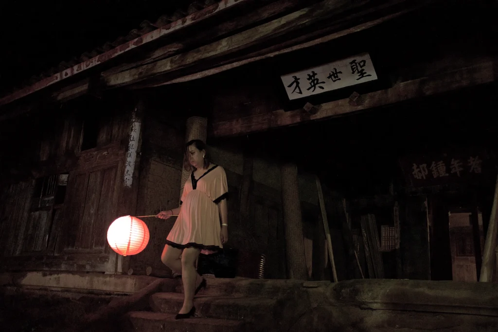 Wan Ying walking away from a rural house holding a red lantern in Sunken Plum